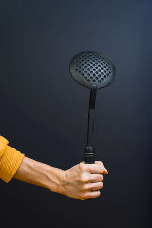 Kitchen accessories. In the hand of a spoon for pasta, close - up on a black background.の写真素材