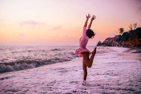 Silhouette of a stunning girl on the beach, on the background of a pink dawn, in the pose of a jumping ballerina on stage, with arms spread in the form of wings.の写真素材