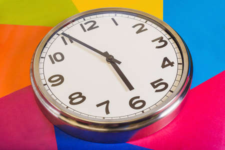 Steel clock on a multicolored background, the hands indicate five minutes to six. Close up. The view from the top. の写真素材