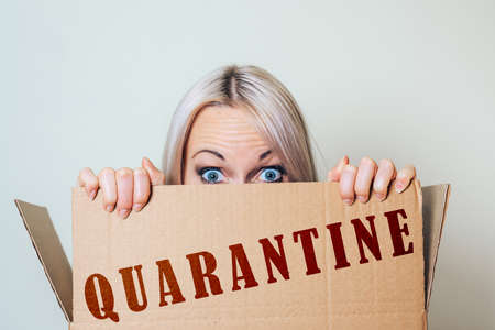 A girl with a panicked look looks out of a box labeled quarantine. The concept of the unexpected spread of the disease.の写真素材