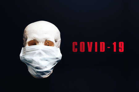 A skull in a medical mask on a black background with the inscription covid-19. The concept of an epidemic , an unknown virus.の写真素材