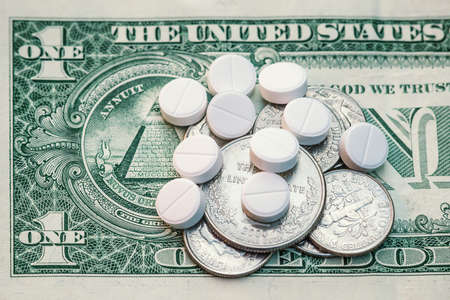 White tablets are lying with small coins on a one- dollar bill. The concept of the cost of medicines , the pharmacological business, and the cost of treatment .の写真素材