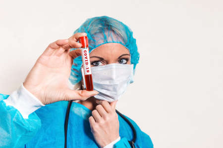 A female doctor looks thoughtfully at a blood tube labeled covid-19. The concept of studying the virus , the search for a vaccineの写真素材