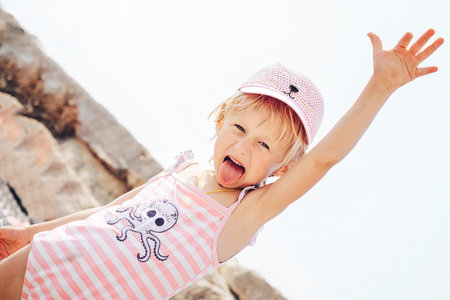 A Jolly little girl in a rose-colored cap stuck out her tongue and held up her hand as she rested on...