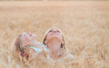 A young mother and daughter are walking, hugging in a field of rye enjoying a wonderful mood and warm weather with their eyes raised high in the sky.の写真素材