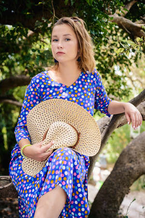 Attractive girl with a straw hat and a blue polka dot dress, on a walk in the Park on vacation near the coast of the sea.の写真素材