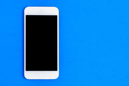 White mobile phone with a black screen on a blue background.の写真素材