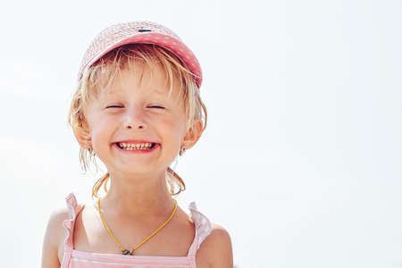 A cheerful, smiling little girl in a rose-colored hat narrowed her eyes with pleasure on a vacation by the sea.の写真素材