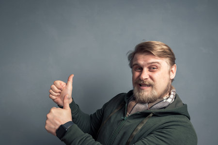 Close-up portrait of a bearded young blond guy with thumbs up on both hands showing cool.の写真素材