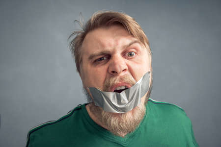 A close-up portrait of a bearded man with his mouth taped shut. The concept of what can't be said is censorship.の写真素材