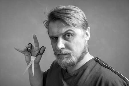 Close-up of a bearded blond man with a pair of scissors in his hand. The concept of self-care for the hair style change and hair salon. black and white photo.の写真素材