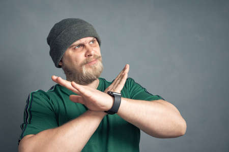 An irritated bearded man crosses his arms in the x sign and looks displeased, which means stop, indicating the final no, this is the end. By no means, the concept of negation.の写真素材