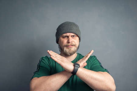 An irritated bearded man crosses his arms in the x sign and looks displeased, which means stop, indicating the final no, this is the end. By no means, the concept of negation.の写真素材
