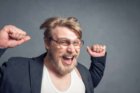 Portrait of a bearded guy with glasses, tousled hair, clenched fists, and a contented face. The concept of luck, leadership and victory, success.の写真素材