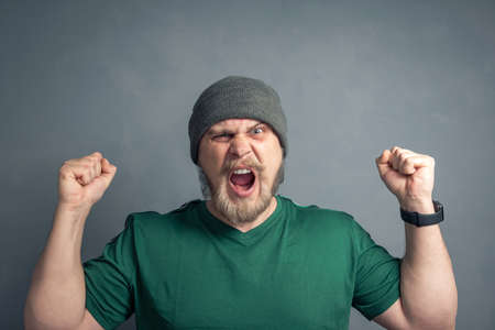 Portrait of a bearded guy with raised hands and clenched fists, shouting Yes. The concept of luck, leadership and victory.の写真素材