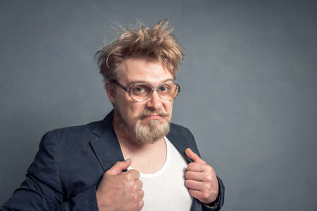 Portrait of a bearded nerd with a disheveled hairstyle, with a thoughtful look looking through his large glasses with a sad face.の写真素材
