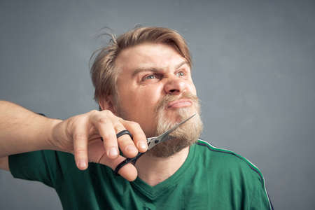 An irritated man wants to cut off his beard with scissors. The concept of changing the style.の写真素材
