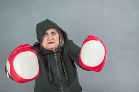 An elderly woman in Boxing gloves on a gray