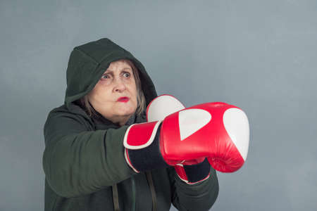 An elderly woman in Boxing gloves on a gray background. The concept of fighting, winning, fighting spirit, sports.の写真素材