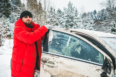 A man after an accident holds on to the door of a crashed car, on the side of the road in winter.の写真素材