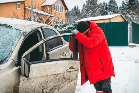 A man after an accident holds on to the door of a crashed car, on the side of the road in winter.の写真素材