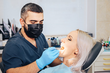 Blonde girl in a dental chair with her mouth open during a doctor's examination.の写真素材