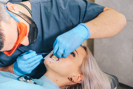 A girl at the reception of a male dentist in a dental chair, with her mouth open during a dental cleaning procedure.の写真素材