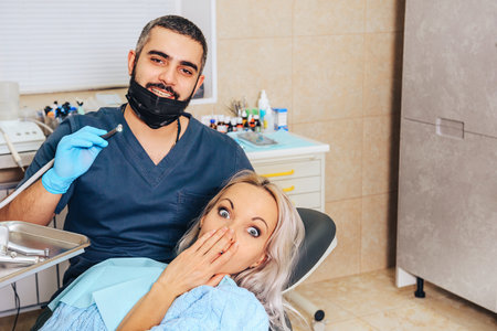 A frightened blonde girl at a reception at a cheerful, smiling dentist.の写真素材