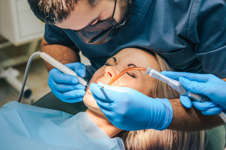 A girl at the reception of a male dentist in a dental chair, with her mouth open during a dental cleaning procedure.の写真素材