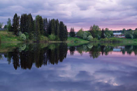 spring rural landscape and flowering shrubs reflected in the evening pondの写真素材