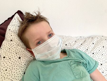a small boy in green clothes is lying on a pillow in a protective mask from the virus.の写真素材