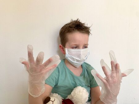 A child in a protective mask looks at his hands in latex, protective gloves.の写真素材