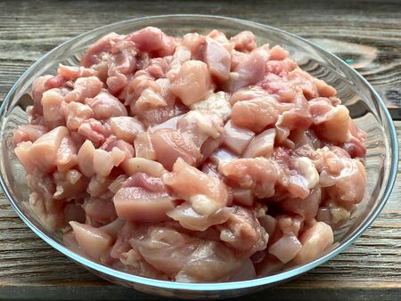 Chicken meat cut into small pieces in a transparent plate, on a wooden background.の写真素材
