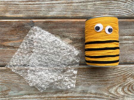 A bee made of wool yarn and a tin can, without wings, with a film with bubbles.の写真素材