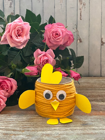 Yellow chicken-Easter craft made from recycled toilet paper, on a background of pink flowers.の写真素材