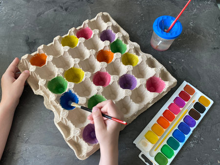 Children's hands paint an empty egg box with paints, recycling, for playing. Hunting for color in...