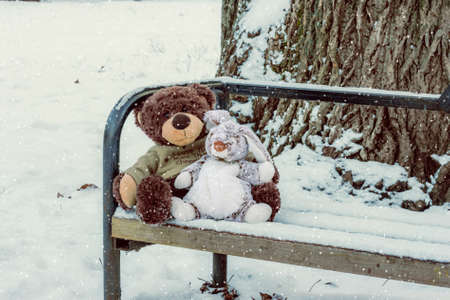Toy bear and a hare sitting on the bench in the snowの写真素材