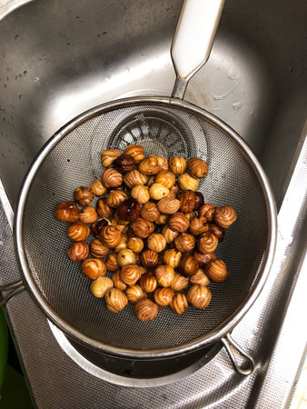 A handful of washed hazelnuts lies in a colander in a metal sink. Beautiful pattern on the surface...