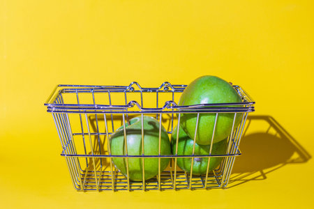 shopping basket with apples,fruit for food,cart supermarket,several objects, green round, metal grate, stands on the surface of the yellow background.concept purchase of apples fruit.の写真素材