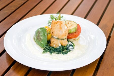 grill fish in roll serve with tomato and yellow and green bell pepper on white plateの写真素材