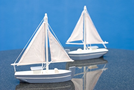 two small blue and white wooden sailboat models on table with blue backgroundの写真素材