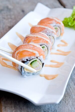 using chopsticks with salmon sashimi roll on white plate topping with cream sauceの写真素材