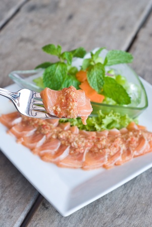 bite of salmon sashimi topping with spicy sauce and fresh mix vegetableの写真素材