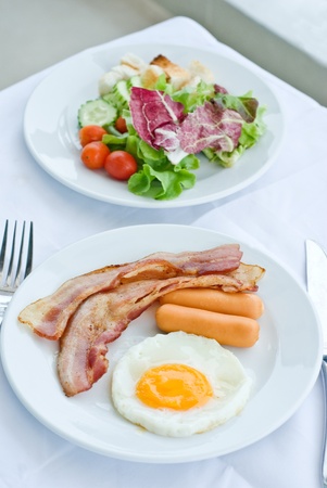 set of American breakfast including fried egg, sausage and bacon and salad on white tableの写真素材