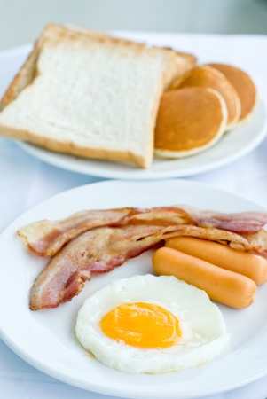 set of American breakfast including fried egg, sausage and bacon serves with bread and pancakes on white tableの写真素材