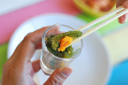 Using chopsticks with Oval sea grapes seaweed and roe in cocktail glassの写真素材