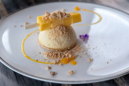 Selective focus of mango cheesecake with crumble on white plateの写真素材