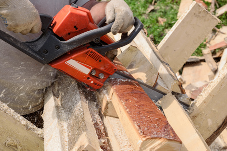 man saws wood with orange chainsawの写真素材