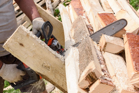 man saws wood with orange chainsaw