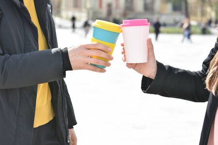 Two women's hands holding stylish reusable eco coffee cups outdoors.の写真素材